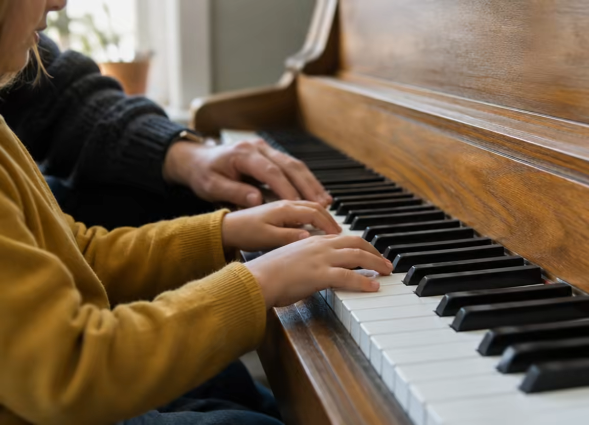 A child's hands on piano keys beside a teacher's guiding hand